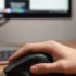 Una mano sostiene un mouse negro frente a una computadora.