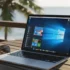 Laptop con pantalla de Windows 10 sobre una mesa junto a un vaso y gafas de sol, con vista al mar y palmeras al fondo.