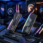 Dos sticks the memoria RAM expuestos encima de una placa base gaming con iluminacion rgb. Y dos PCs gaming de fondo.