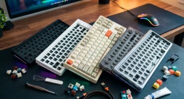 Varios kits de teclado mecánico barebone en diferentes colores y tamaños sobre un escritorio, acompañados de interruptores, teclas de colores, herramientas de montaje y lubricante para armar un teclado personalizado económico.