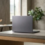 Portátil gris cerrado sobre una mesa de hormigón en una oficina moderna con estanterías de madera al fondo. Imagen generada con IA.