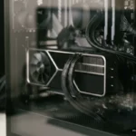 Interior de caja de ordenador con tarjeta gráfica de doble ventilador y cables trenzados negros conectados. Imagen generada con IA.