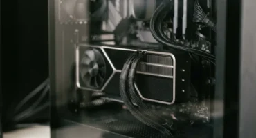 Interior de caja de ordenador con tarjeta gráfica de doble ventilador y cables trenzados negros conectados. Imagen generada con IA.