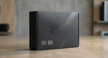 Caja negra de cartón sobre una mesa de madera con diseño geométrico en relieve y dos iconos pequeños en la parte frontal inferior. Imagen generada con IA.