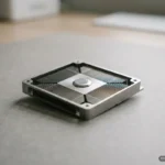 Disipador de calor de aluminio con aletas de ventilación y tornillo central sobre superficie gris. Imagen generada con IA.