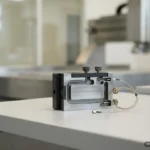 Dispositivo de medición con pantalla analógica, dos botones de ajuste y un cable conectado, sobre una mesa de laboratorio. Imagen generada con IA.