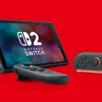 Consola Nintendo Switch 2 apoyada en su soporte sobre fondo rojo, con el logotipo en pantalla y dos Joy-Con delante