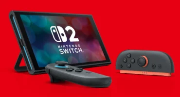 Consola Nintendo Switch 2 apoyada en su soporte sobre fondo rojo, con el logotipo en pantalla y dos Joy-Con delante
