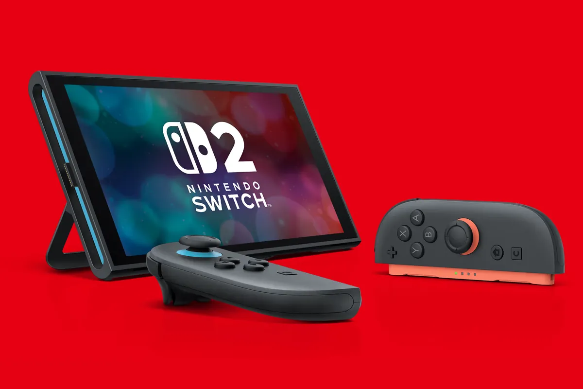 280-nintendo-switch-2-revision-ue-bateria-mas-pequena-1 Consola Nintendo Switch 2 apoyada en su soporte sobre fondo rojo, con el logotipo en pantalla y dos Joy-Con delante