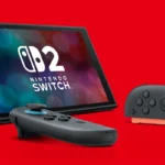 Consola Nintendo Switch 2 apoyada en su soporte sobre fondo rojo, con el logotipo en pantalla y dos Joy-Con delante