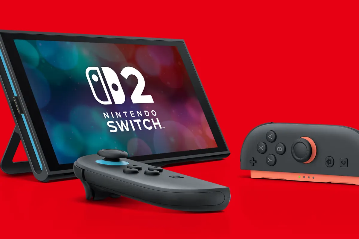 280-nintendo-switch-2-revision-ue-bateria-mas-pequena Consola Nintendo Switch 2 apoyada en su soporte sobre fondo rojo, con el logotipo en pantalla y dos Joy-Con delante