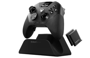 395-steelseries-aeon-pro-mando-pc-xbox-quickswitch Mando SteelSeries Aeon Pro negro sobre su base QuickSwitch, con la pantalla OLED encendida y dos baterías de repuesto al lado