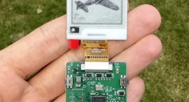 Placa verde con pantalla de tinta electrónica sostenida en una mano sobre césped