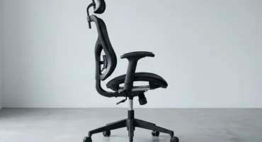 Silla de oficina de malla vista de perfil, con el mecanismo del asiento, el pistón y la base de cinco radios a la vista. Imagen generada con IA.