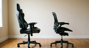 Una silla gaming y una silla de oficina de malla, las dos negras, una junto a otra en una habitación vacía. Imagen generada con IA.
