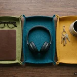 Tres bandejas de fieltro de colores con gafas y libreta, unos auriculares y llaves con una taza. Imagen generada con IA.