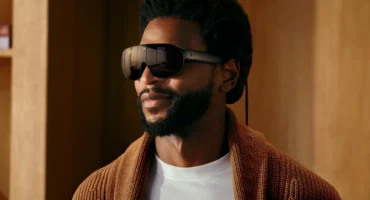 Un hombre con barba lleva las Meta VR Glasses, unas gafas oscuras de realidad virtual con un cable, en una habitación de madera