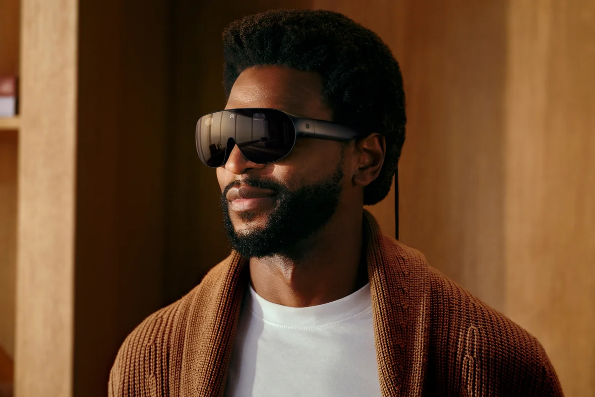 meta-vr-glasses Un hombre con barba lleva las Meta VR Glasses, unas gafas oscuras de realidad virtual con un cable, en una habitación de madera