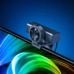 La webcam Razer Kiyo V2 Pro, negra y con el objetivo redondo, colocada sobre el borde de un monitor con un fondo de colores