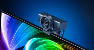 La webcam Razer Kiyo V2 Pro, negra y con el objetivo redondo, colocada sobre el borde de un monitor con un fondo de colores