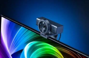 La webcam Razer Kiyo V2 Pro, negra y con el objetivo redondo, colocada sobre el borde de un monitor con un fondo de colores