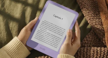 Unas manos sostienen un Kindle lila con el primer capítulo de un libro en castellano en la pantalla, sobre una manta de punto