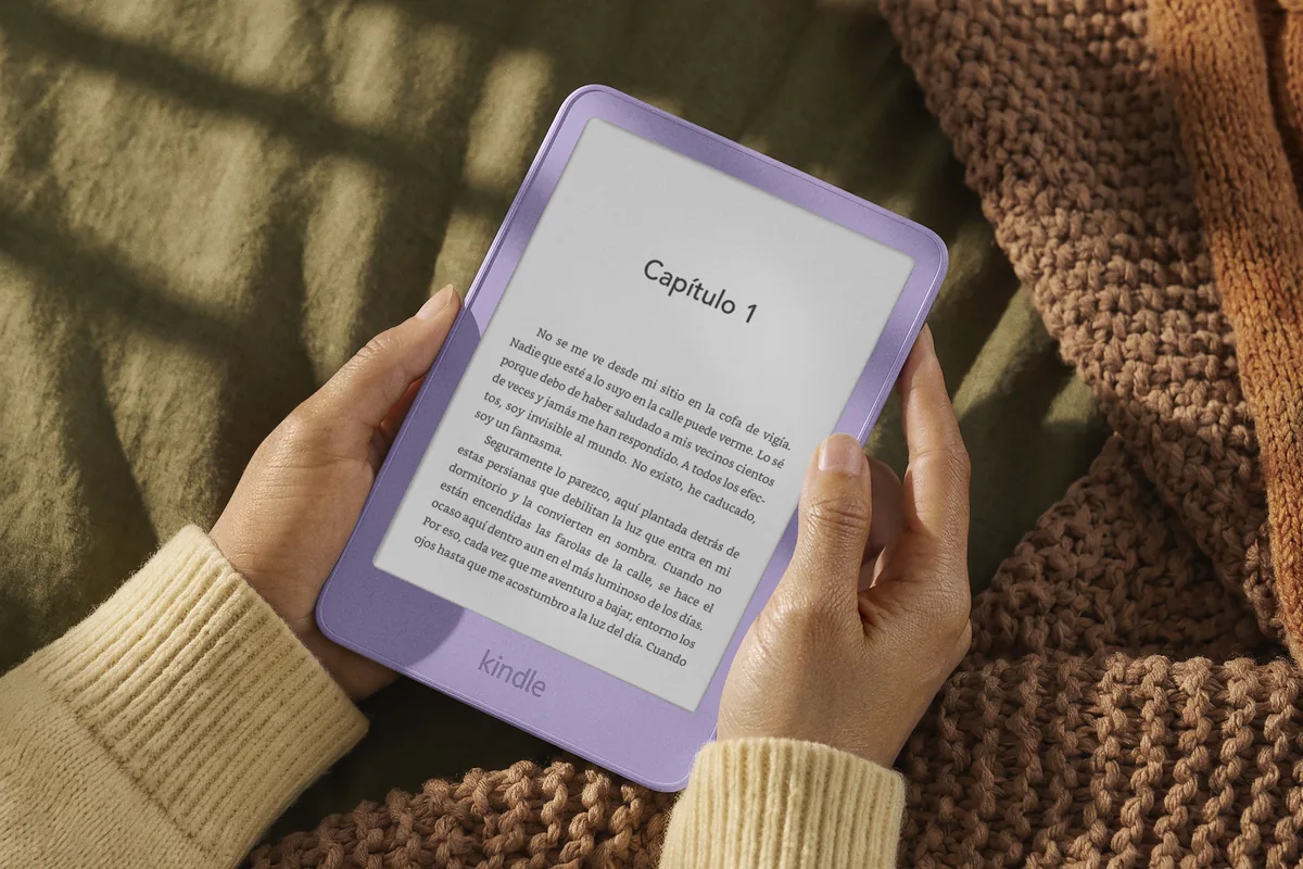 amazon-gama-kindle-redisenada Unas manos sostienen un Kindle lila con el primer capítulo de un libro en castellano en la pantalla, sobre una manta de punto