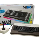 THE 800XL de Retro Games, con su teclado marrón y crema, delante de su caja y junto al joystick THECXSTICK