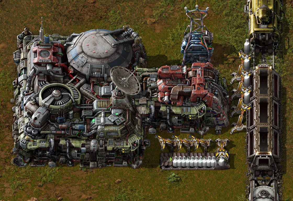 Plataforma de aterrizaje de Factorio vista desde arriba, con su bahía de descarga: los insertadores sacan frascos a una cinta y a los vagones de un tren