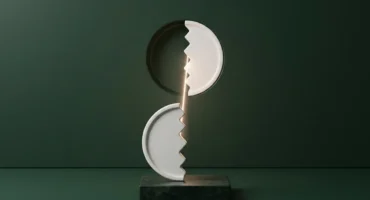 Un medallón de cerámica blanca partido en dos con borde en zigzag: una mitad sobre un pedestal de piedra y la otra encajada en un muro verde, unidas por un hilo de luz. Imagen generada con IA.