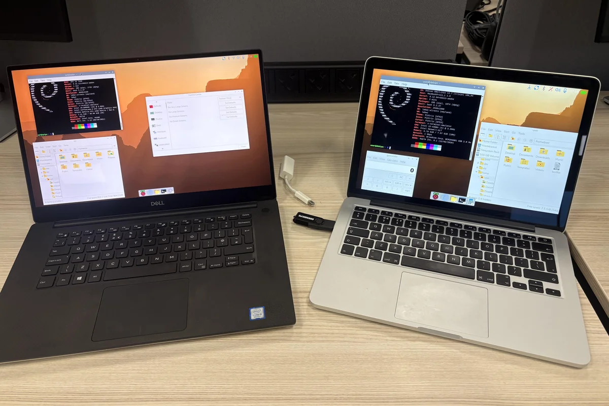 raspberry-pi-desktop-pc-mac Un portátil Dell XPS y un MacBook Pro sobre una mesa de madera, los dos con el escritorio de Raspberry Pi y una memoria USB conectada al MacBook