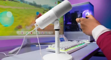 El micrófono Shure MV6 Gen 2 en blanco, sobre su soporte de escritorio, junto a un teclado, un monitor con un juego y un PC con iluminación morada