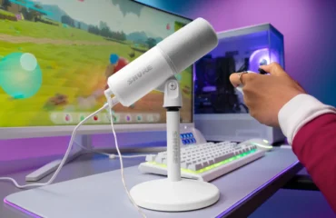 shure-mv6-gen-2-blanco El micrófono Shure MV6 Gen 2 en blanco, sobre su soporte de escritorio, junto a un teclado, un monitor con un juego y un PC con iluminación morada