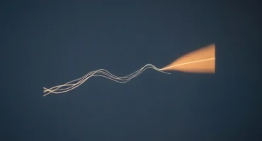 Líneas finas y luminosas que ondulan sobre un fondo azul oscuro y terminan en un abanico naranja, como una gráfica con su previsión. Imagen generada con IA.