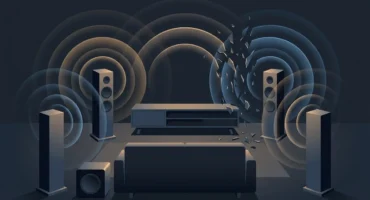 Salón en penumbra con sofá, cuatro altavoces de columna y un subwoofer sin marcas que emiten ondas de sonido, rotas en un lado. Imagen generada con IA.
